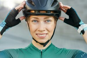 Portrait of cheerful young woman, female cyclist putting on biking helmet, smiling at camera while